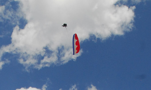 Piloto passa sobre o parapente vermelho durante uma Espiral Assimétrica