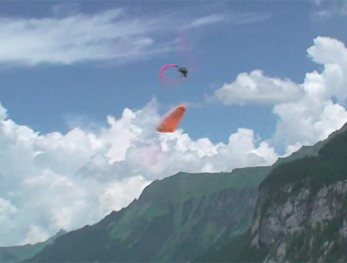 Parapente laranja realiza um Infinity Tumbling com montanhas ao fundo