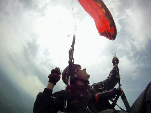 Parapente vermelho estabiliza sobre a cabeça do piloto abordo