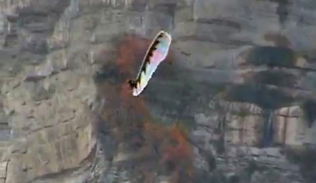 Parapente branco realizando um Misty Flip para a direita com paredão de montanha ao fundo